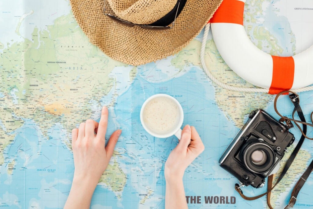 person looking at world map with hat, camera, and coffee on top